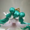 فیگور انیمه هاتسونه میکو ایستاده روی پایه گل‌دار، با لباس سفید و موهای بلند سبز